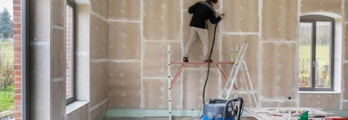 Eine Person schleift eine Trockenbauwand mit einer Schleifmaschine.